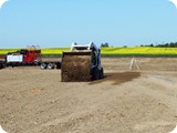 Once wall package corners are pinned and marked, the Bobcat operator begins spreading base screenings (aggregate) below the geotextile matting and liner.