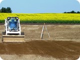 Once wall package corners are pinned and marked, the Bobcat operator begins spreading base screenings (aggregate) below the geotextile matting and liner.