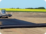 The crew rolls out the geotextile matting while the Bobcat operator sets the liner in place to be unfolded above the geotextile.