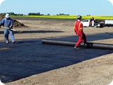 The crew rolls out the geotextile matting while the Bobcat operator sets the liner in place to be unfolded above the geotextile.